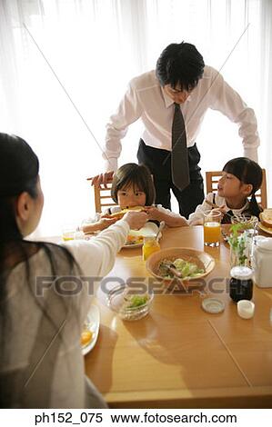 Two girls and their mother sitting at a dining table with their father standing behind them View Large Photo Image Stock Photography - Two girls and their mother sitting at a dining table with their father standing behind them. Fotosearch