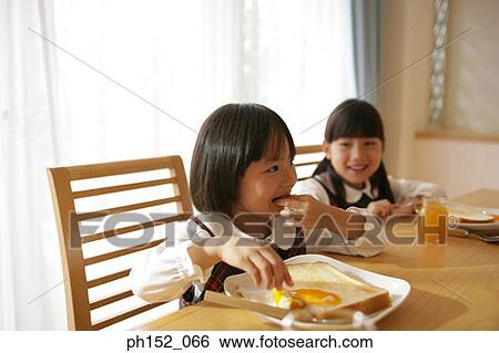 Stock Photograph - Two girls having breakfast at the dining table. Fotosearch
