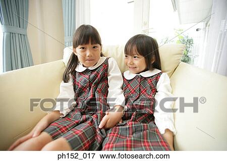 Stock Photo - Two girls holding hands and sitting on a couch. Fotosearch