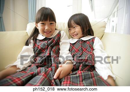 Stock Photo - Two girls holding hands and sitting on a couch. Fotosearch