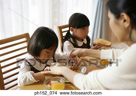 Picture - Two girls sitting at the dining table with their mother serving breakfast. Fotosearch