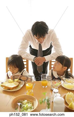 Two girls sitting at the dining table with their father leaning against their chairs View Large Photo Image Stock Image - Two girls sitting at the dining table with their father leaning against their chairs. Fotosearch