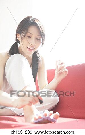 Stock Photography - Close-up of a young woman applying nail polish on her toenails. Fotosearch