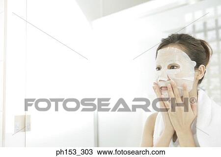 Stock Image - Close-up of a young woman applying paper facial mask. Fotosearch