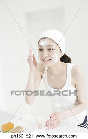 Stock Image - Close-up of a young woman applying moisturizer on her face. Fotosearch