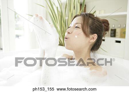 Stock Photography - Close-up of a young woman blowing foam in a bubble bath. Fotosearch
