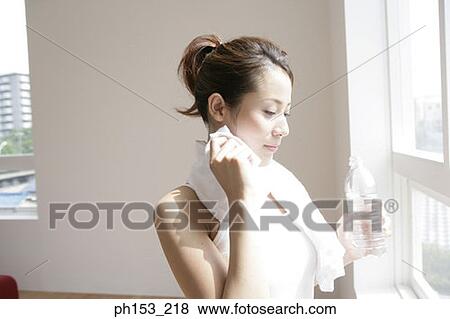 Close-up of a young woman holding a water bottle and wiping her face with a towel View Large Photo Image Stock Photo - Close-up of a young woman holding a water bottle and wiping her face with a towel. Fotosearch
