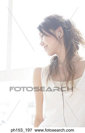 Stock Photo - Close-up of a young woman listening to music and smiling. Fotosearch