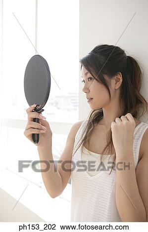 Close-up of a young woman looking in a hand mirror and touching her hair View Large Photo Image Stock Image - Close-up of a young woman looking in a hand mirror and touching her hair. Fotosearch