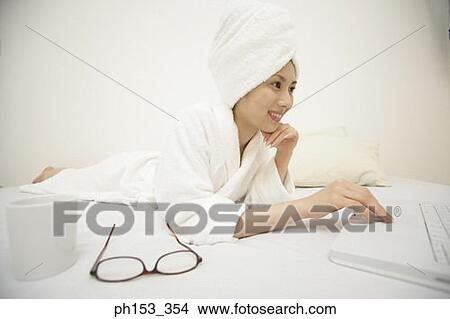 Close-up of a young woman lying on the bed and using a laptop View Large Photo Image Picture - Close-up of a young woman lying on the bed and using a laptop. Fotosearch