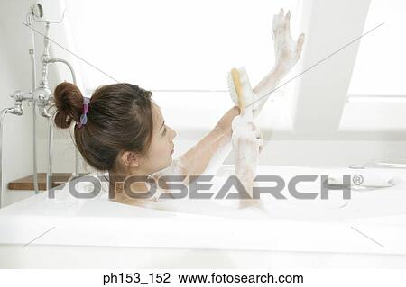 Stock Image - Close-up of a young woman scrubbing her arm with a brush in a bathtub. Fotosearch