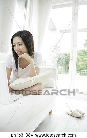 Close-up of a young woman sitting on a couch and using a laptop View Large Photo Image Picture - Close-up of a young woman sitting on a couch and using a laptop. Fotosearch
