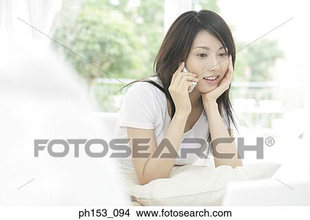 Close-up of a young woman sitting on a couch and talking on a mobile phone View Large Photo Image Picture - Close-up of a young woman sitting on a couch and talking on a mobile phone. Fotosearch