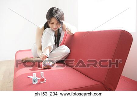 Close-up of a young woman sitting on a couch and applying nail polish View Large Photo Image Picture - Close-up of a young woman sitting on a couch and applying nail polish. Fotosearch