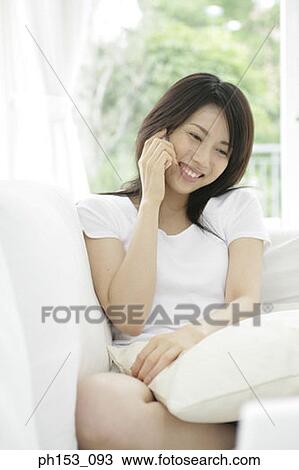 Close-up of a young woman sitting on a couch and talking on a mobile phone View Large Photo Image Stock Image - Close-up of a young woman sitting on a couch and talking on a mobile phone. Fotosearch