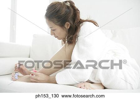 Close-up of a young woman sitting on a couch and applying ...