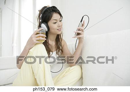 Stock Photo - Close-up of a young woman sitting on a couch and listening to music. Fotosearch