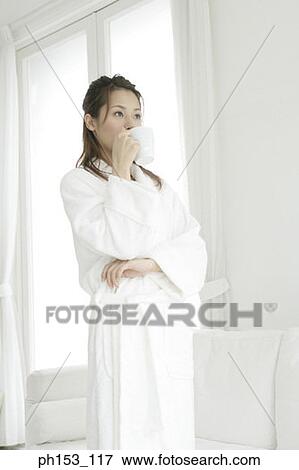 Stock Photo - Close-up of a young woman standing and drinking a cup of coffee. Fotosearch