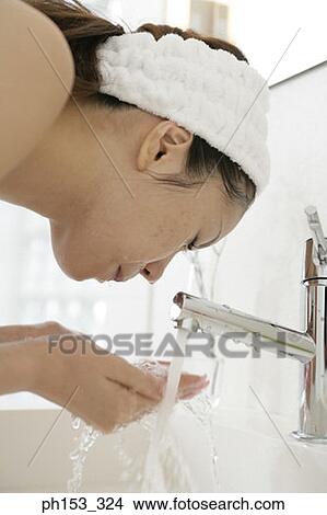 Picture - Close-up of a young woman washing her face over a bathroom sink. Fotosearch