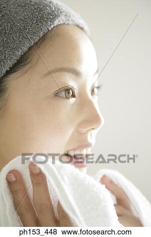 Close-up of a young woman wiping her face with a towel and smiling View Large Photo Image Stock Photo - Close-up of a young woman wiping her face with a towel and smiling. Fotosearch