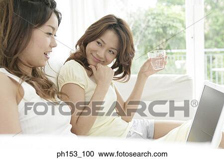 Close-up of two young women sitting on a couch and using a laptop View Large Photo Image Stock Image - Close-up of two young women sitting on a couch and using a laptop. Fotosearch