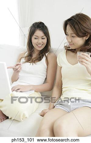 Stock Image - Close-up of two young women sitting on a couch and using a laptop. Fotosearch