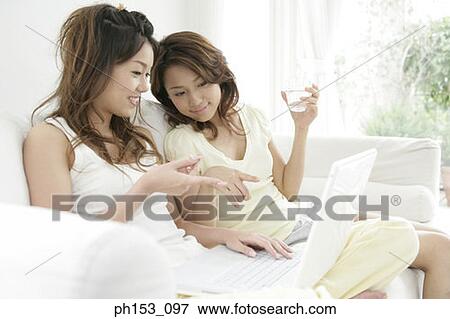 Stock Photo - Close-up of two young women sitting on a couch and using a laptop. Fotosearch