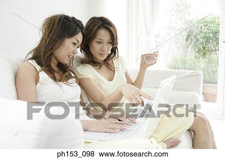 Close-up of two young women sitting on a couch and using a laptop View Large Photo Image Stock Photo - Close-up of two young women sitting on a couch and using a laptop. Fotosearch