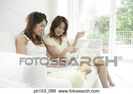 Close-up of two young women sitting on a couch and using a laptop View Large Photo Image Stock Photo - Close-up of two young women sitting on a couch and using a laptop. Fotosearch