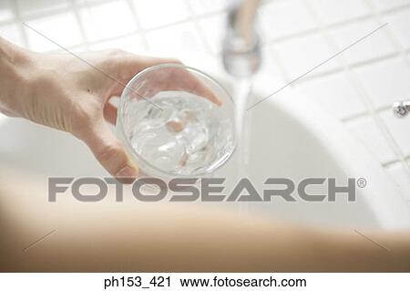 High angle view of a woman's hand filling water into a glass from a faucet View Large Photo Image Stock Image - High angle view of a woman's hand filling water into a glass from a faucet. Fotosearch