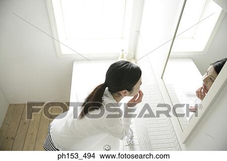 Picture - High angle view of a young woman looking in a mirror and touching her lips. Fotosearch