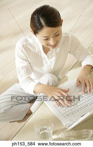 High angle view of a young woman sitting on the floor and using a laptop on a couch View Large Photo Image Picture - High angle view of a young woman sitting on the floor and using a laptop on a couch. Fotosearch