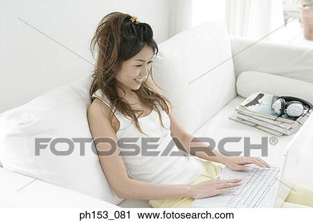 High angle view of a young woman reclining on a couch and using a laptop View Large Photo Image Stock Image - High angle view of a young woman reclining on a couch and using a laptop. Fotosearch