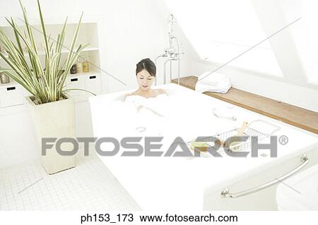 Stock Image - High angle view of a young woman relaxing in a bubble bath. Fotosearch