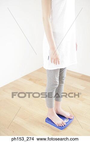 Low section view of a woman standing on a weighing scale View Large Photo Image Picture - Low section view of a woman standing on a weighing scale. Fotosearch