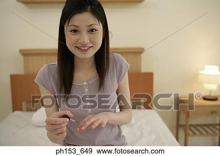 Portrait of a young woman applying nail polish on her fingernails View Large Photo Image Stock Photo - Portrait of a young woman applying nail polish on her fingernails. Fotosearch