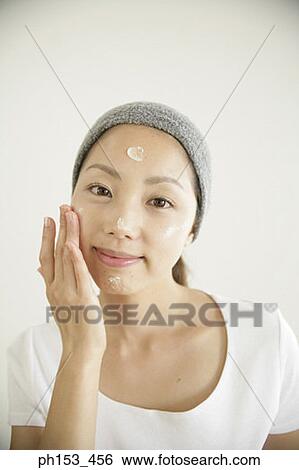 Portrait of a young woman applying moisturizer on her face View Large Photo Image Stock Photograph - Portrait of a young woman applying moisturizer on her face. Fotosearch