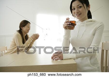 Stock Image - Portrait of a young woman drinking black tea and smiling with her sister. Fotosearch