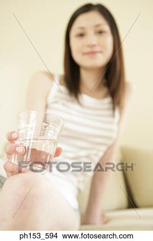 Portrait of a young woman holding a glass of water and smiling View Large Photo Image Picture - Portrait of a young woman holding a glass of water and smiling. Fotosearch