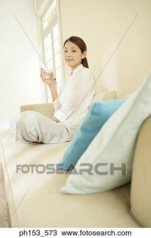 Portrait of a young woman listening to music on a couch and holding a glass of water View Large Photo Image Stock Image - Portrait of a young woman listening to music on a couch and holding a glass of water. Fotosearch