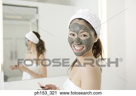 Stock Image - Portrait of a young woman smiling with a facial mask. Fotosearch