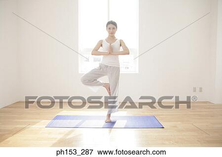 Stock Photo - Portrait of a young woman standing in a tree pose. Fotosearch