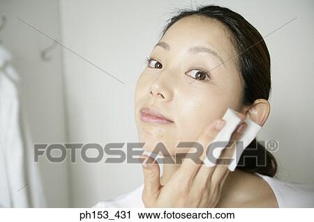 Stock Image - Portrait of a young woman wiping her cheek with a tissue paper. Fotosearch