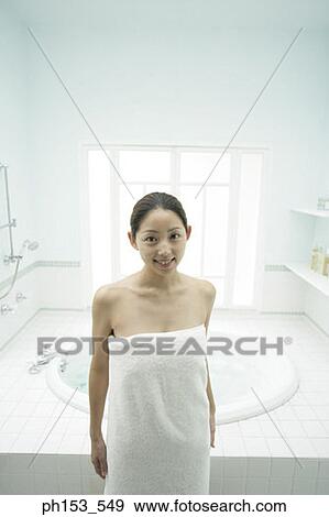 Stock Photo - Portrait of a young woman wrapped in a towel and standing in the bathroom. Fotosearch