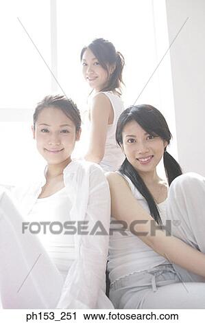 Stock Image - Portrait of three young women sitting together and smiling. Fotosearch