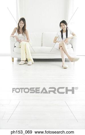 Stock Photo - Portrait of two young women sitting on a couch and smiling. Fotosearch