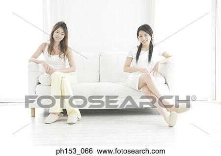 Portrait of two young women sitting on a couch and smiling View Large Photo Image Stock Photograph - Portrait of two young women sitting on a couch and smiling. Fotosearch