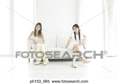 Portrait of two young women sitting on a couch and smiling View Large Photo Image Stock Photography - Portrait of two young women sitting on a couch and smiling. Fotosearch