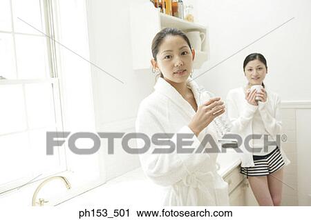 Stock Image - Portrait of two young women standing in the kitchen. Fotosearch