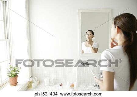 Rear view of a young woman applying face powder on her face in front of a mirror View Large Photo Image Picture - Rear view of a young woman applying face powder on her face in front of a mirror. Fotosearch